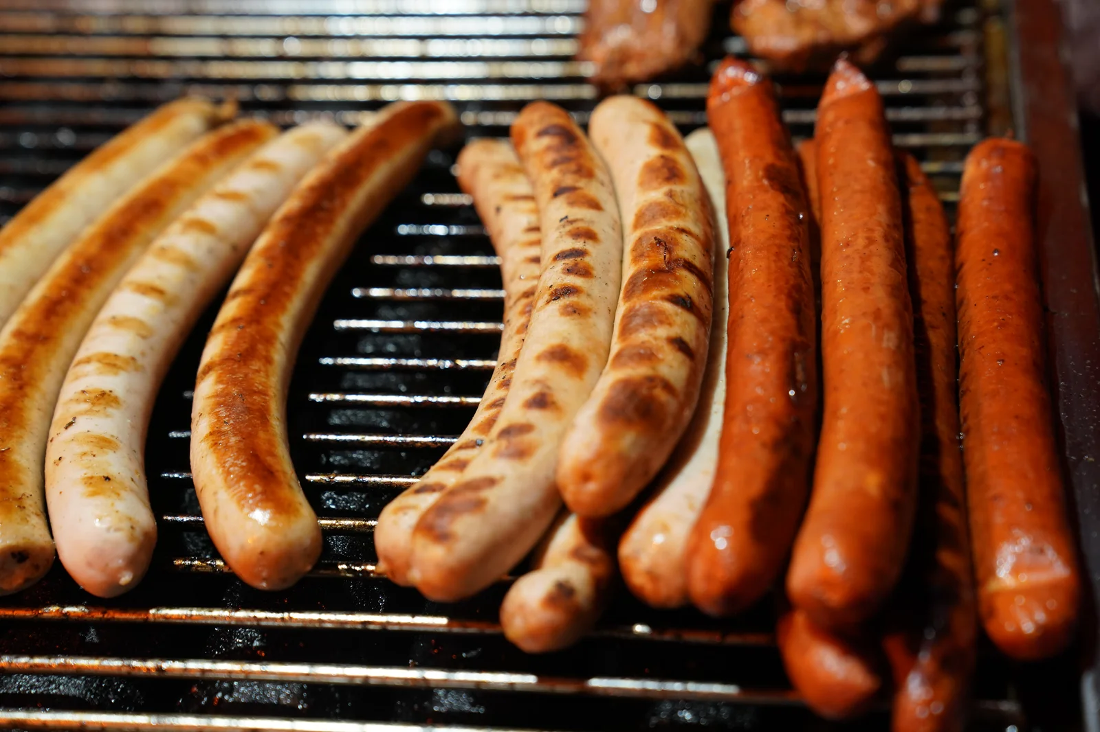 Mehrere Bratwürste und Würstchen liegen nebeneinander auf einem Grill.