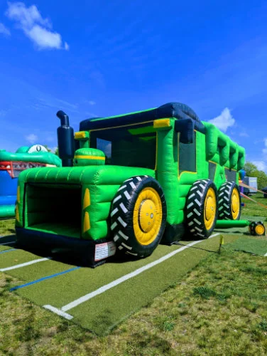 Grüne Traktorhüpfburg mit großen schwarzen Rädern vor blauem Himmel.