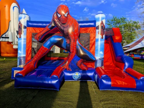 Hüpfburg mit Spiderman Motiv und Rutsche auf einer Wiese.