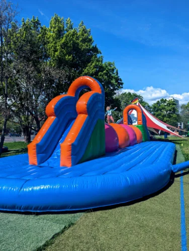 Blau orange Doppelrutsche mit spielenden Kindern auf einer Rasenfläche.